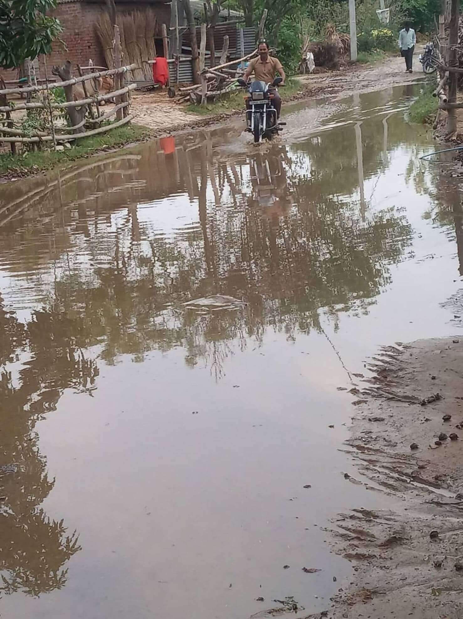 टूटी हुई सड़क पर भरा बारिश का पानी।