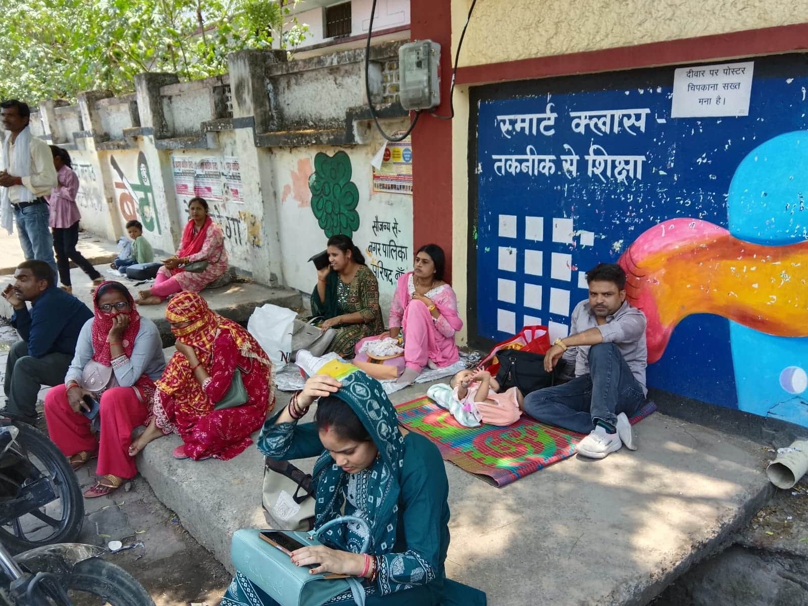 फोटो - 10 तेज धूप से बचने के लिए परीक्षा केंद्र के बाहर पेड़ की छांव में अपने बच्चे के साथ बैठे