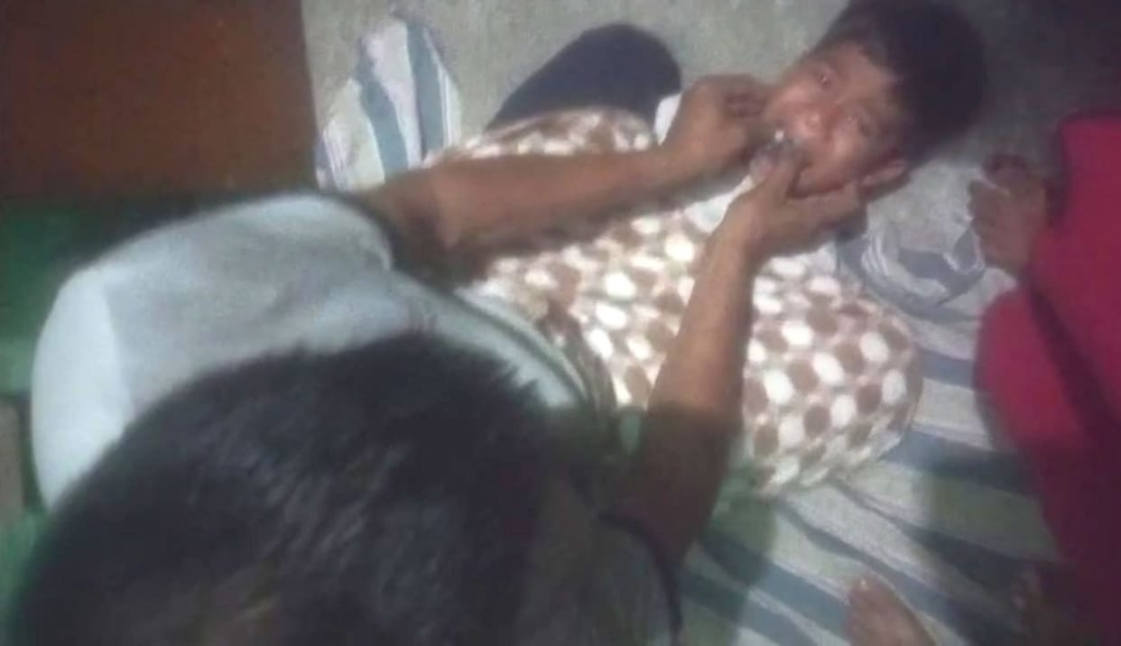 A father sits over his seven-year-old son with a cloth stuffed in his mouth.
