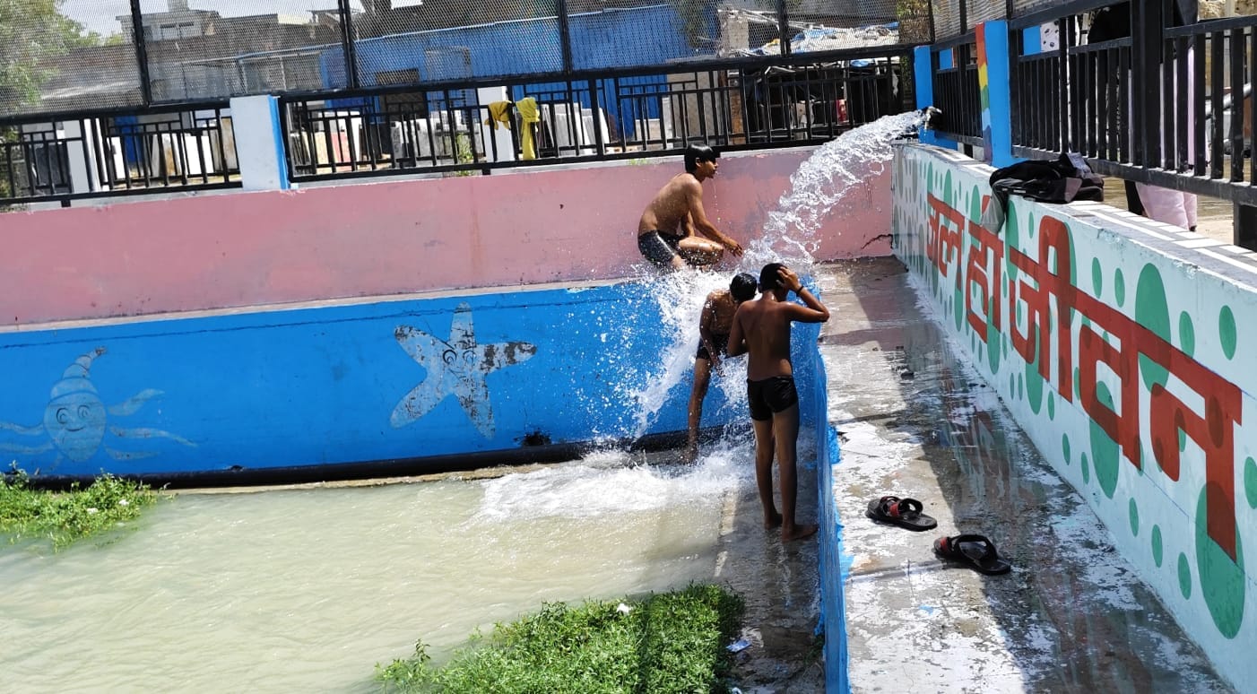 चिलचिलाती धूप में मंझनपुर स्थित तालाब में पंप के गिर रहे पानी से नहाते बच्चे। संवाद