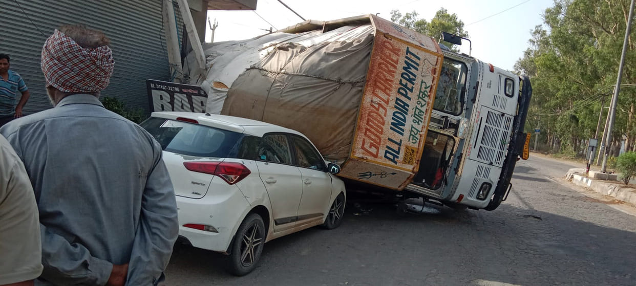 A truck loaded with straw overturned on a car due to potholes, the driver narrowly escaped.
