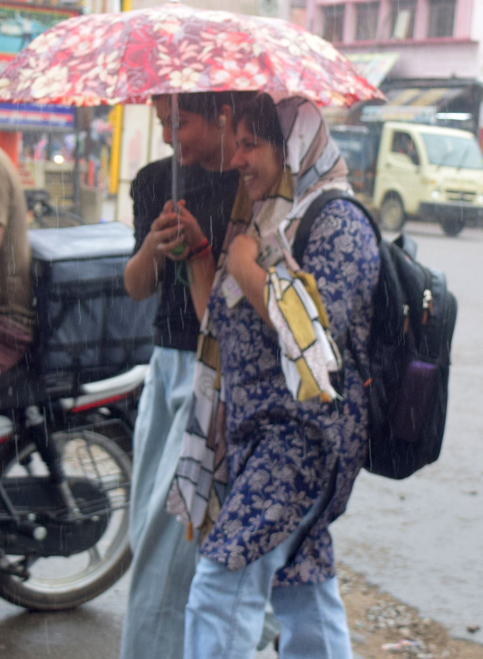 बारिश से बचने के लिए छाता लगाकर जाती युवतियां। 