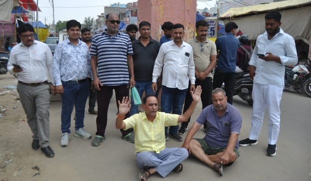 रामलीला मैदान में सड़क पर बैठकर प्रदर्शन करते रामलीला समिति के पदाधिकारी। संवाद