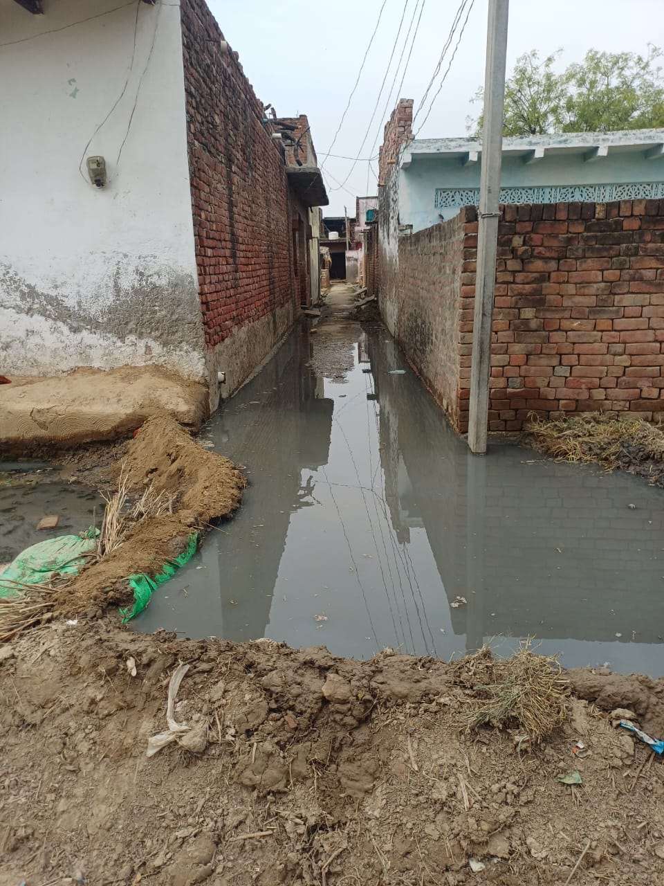 Waterlogging on the road due to the drain being blocked by a wall.