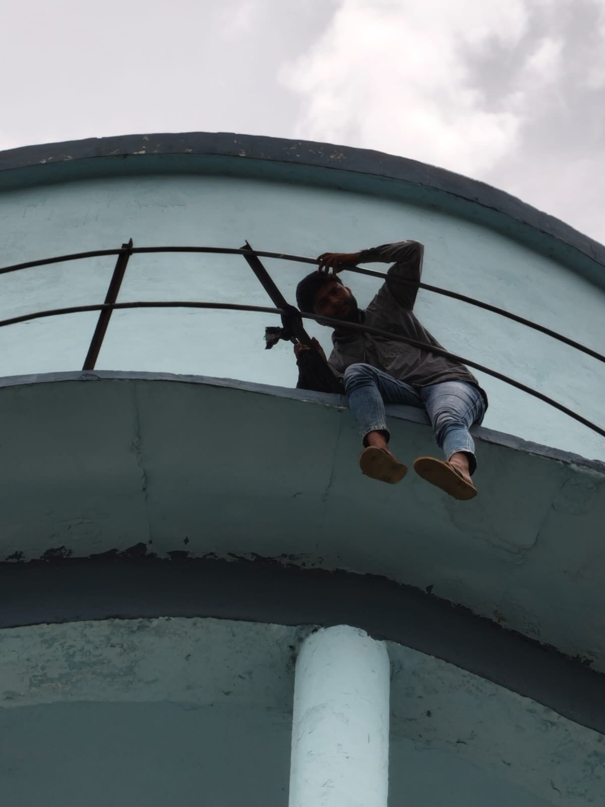 Youth climbs overhead tank after encroachment on village community land is not removed.