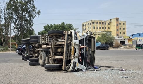 Container trailer overturns while trying to avoid passenger bus; driver critically injured.