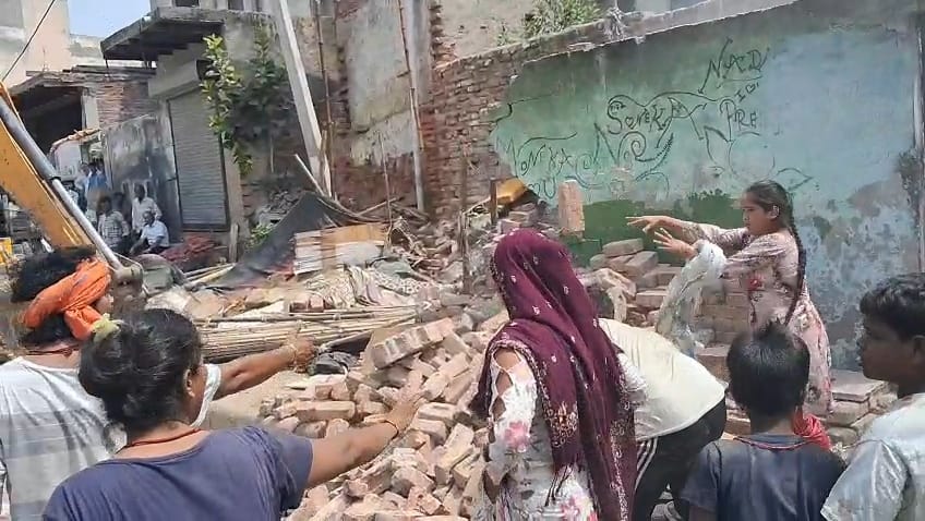 फोटो-65: नगर परिषद की कार्रवाई के दौरान जेसीबी के आगे अड़कर विरोध स्वरूप ईंट उठाकर फेंकती महिला।