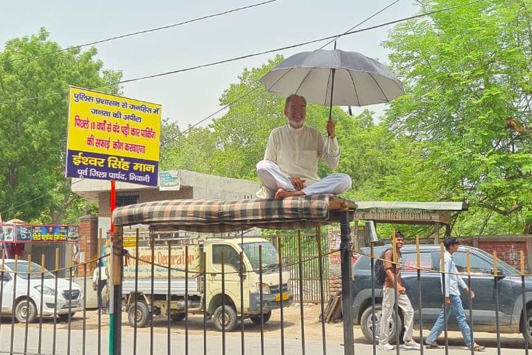 A former councilor staged a sit-in protest by setting up a platform on the sharp-edged grill of a road divider.