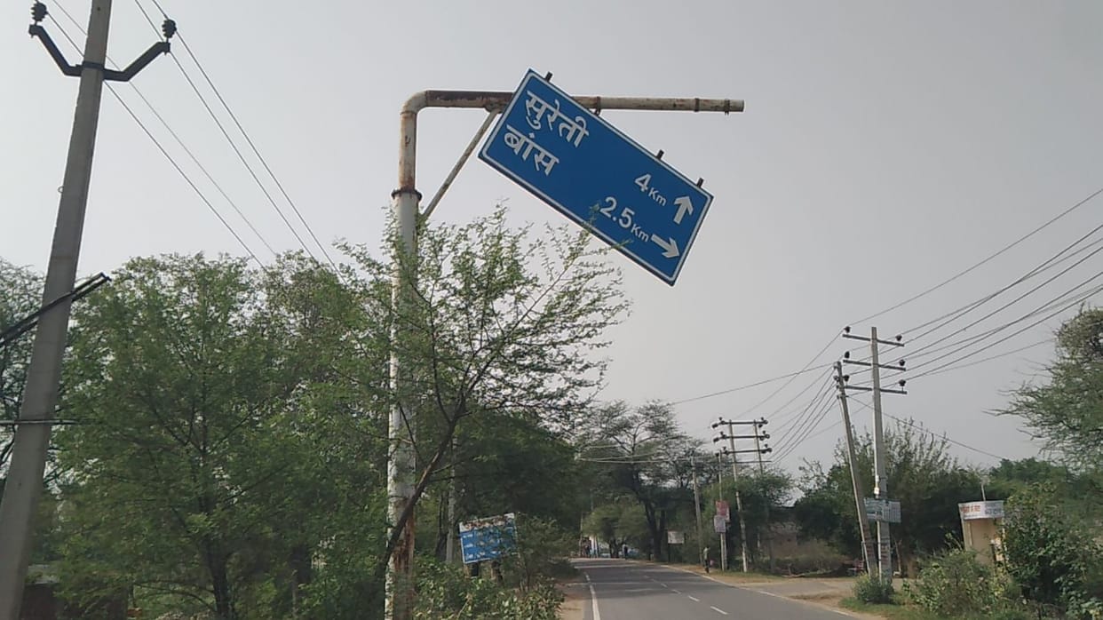 Direction sign tilted by storm on Satnali-Mahendragarh Road; risk of accidents increases.