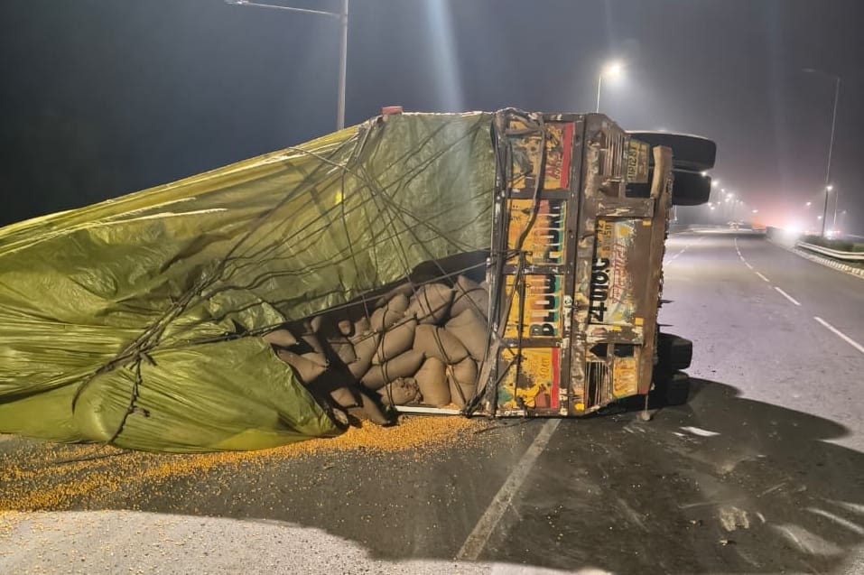 Maize-laden truck overturns on highway after going out of control; grain spills onto the road.