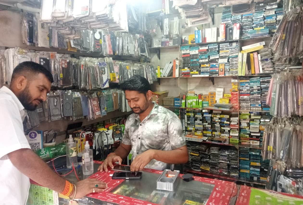 मोबाइल की  रिपेयरिंग करता दुकानदार। संवाद