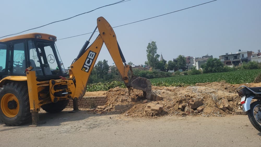JCB arrives to breach pond embankment; villagers protest.