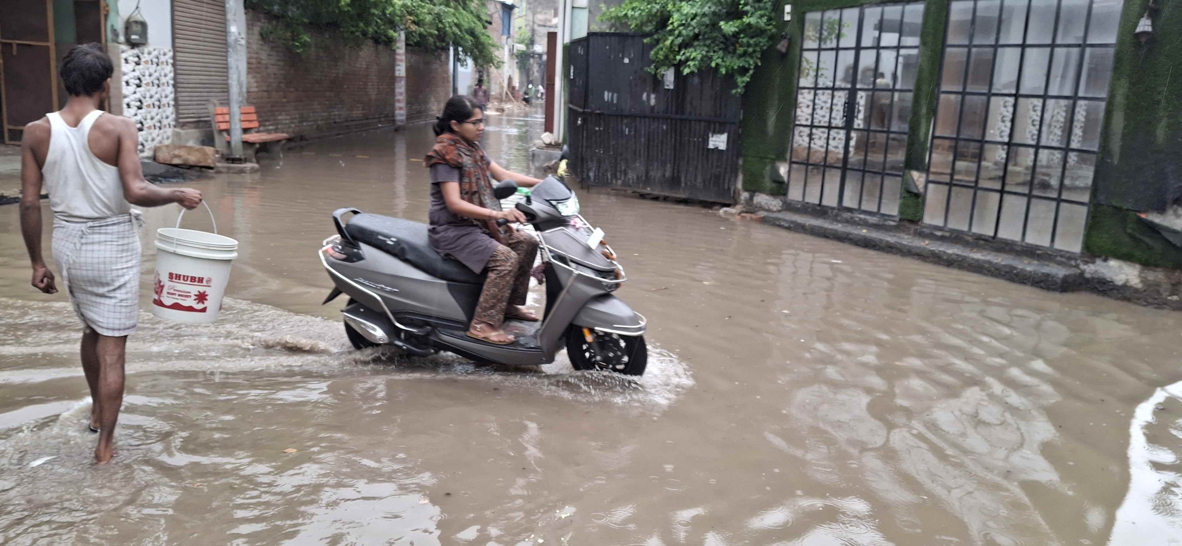 -फोटो 84 : शहर के धर्म विहार में बारिश के भरे पानी के बीच से स्कूटी पर सवार होकर गंतव्य की ओर ज