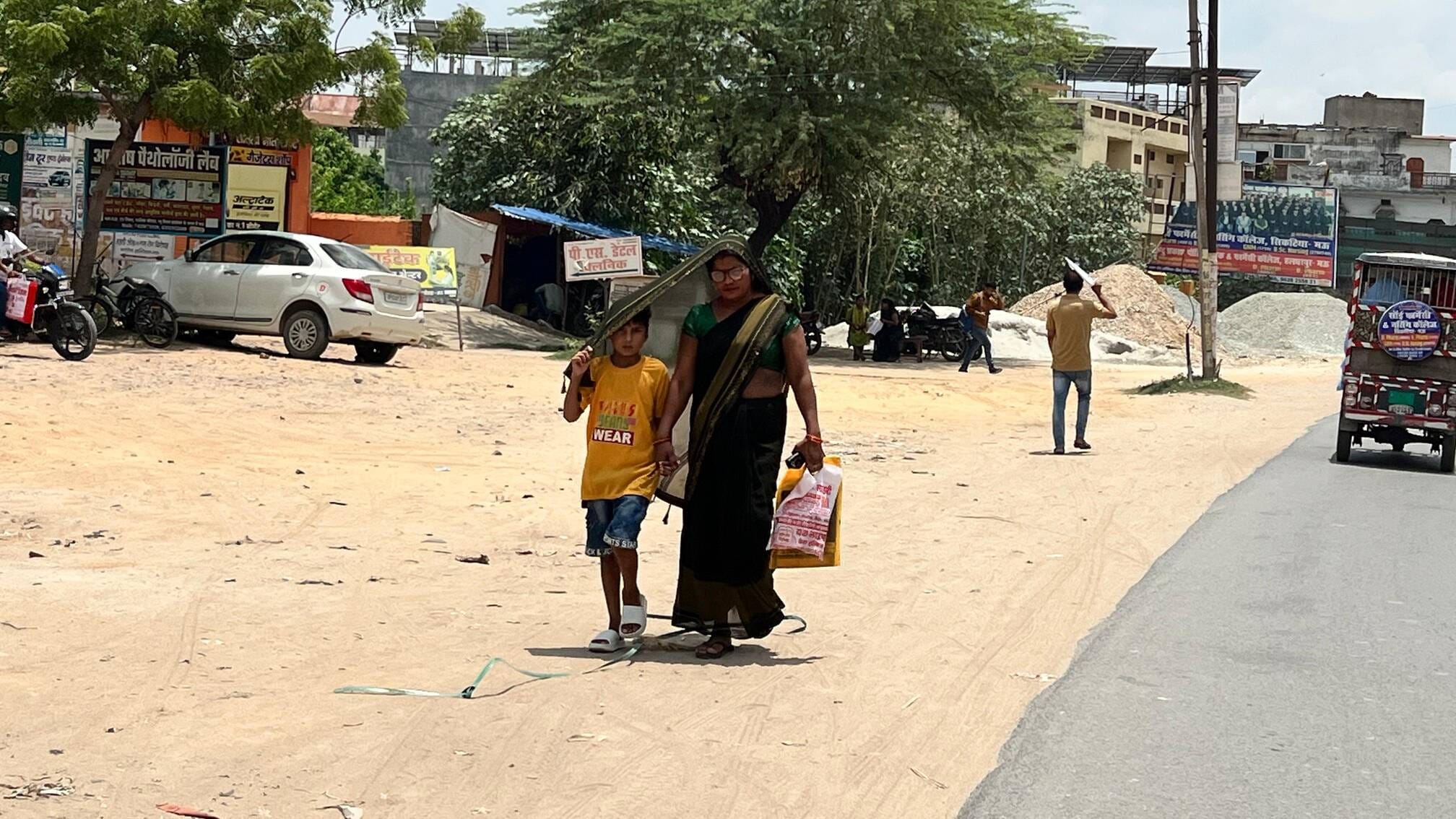 माँ का आँचल:नगर में बृहस्पतिवार को धूप से बचने के लिए अपनी माँ का आँचल से सिर ढक कर जाता बालक।स