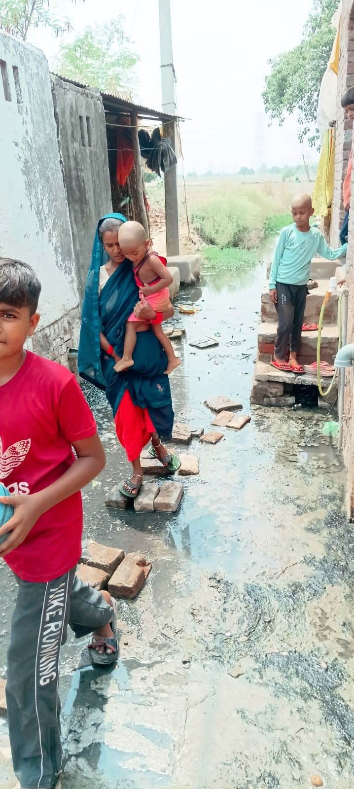 फोटो-12- गली में भरे पानी में ईंट रखकर निकलते बच्चे व महिला।संवाद