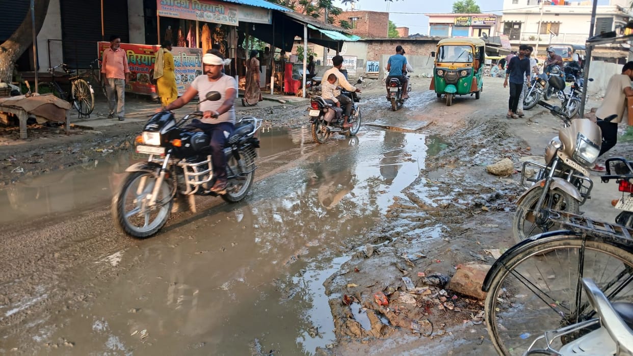 Water accumulates on the road due to the lack of a drain; traders and passersby face inconvenience.
