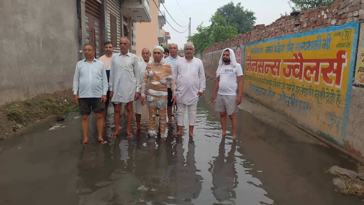 Following a sewer overflow, a district councilor staged a protest alongside residents, wrapping themselves in polythene sheets and tape.