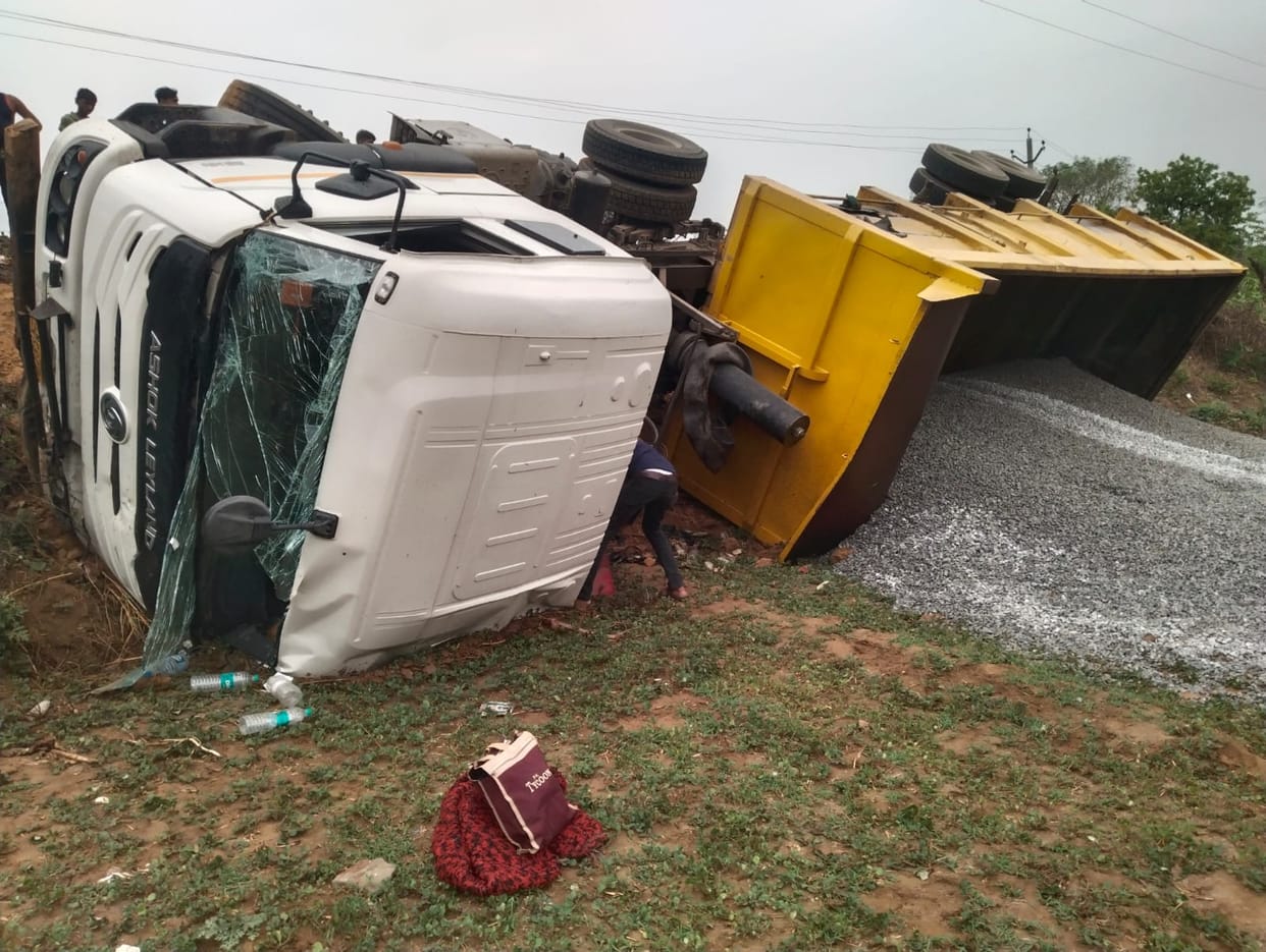 Overloaded truck filled with gravel overturns; bike riders have a narrow escape.