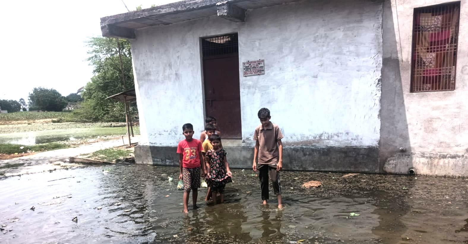 फोटो -3- तालाब ओवर फ्लो होने से गली में भरे गंदे पानी के बीच से निकलते बच्चे। स्रोत:सभासद