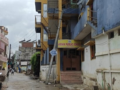 Electricity pole leaning against the school veranda; high-tension wire dangling near the field.
