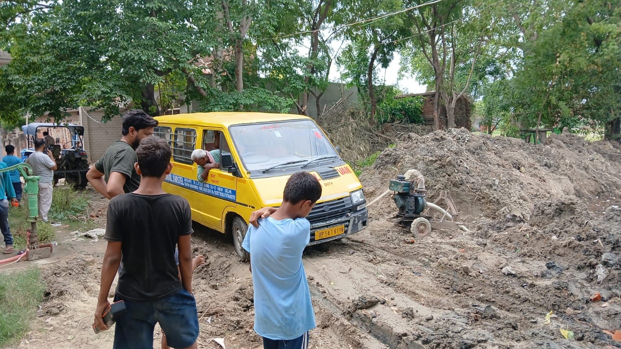 Soil left on the road after drain excavation; school bus gets stuck.