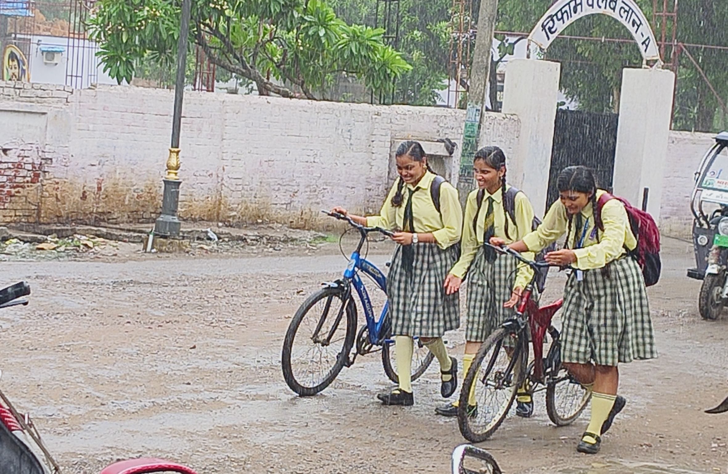 जिला अस्पताल चौराहा के पास उमस भरी गर्मी के बीच हुई हल्की बारिश में भीगते हुए जाती छात्राएं।
