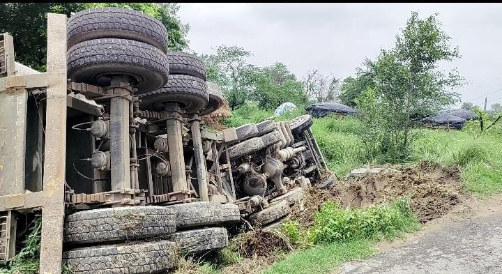 Sand-laden truck overturns onto poles while trying to save a container.
