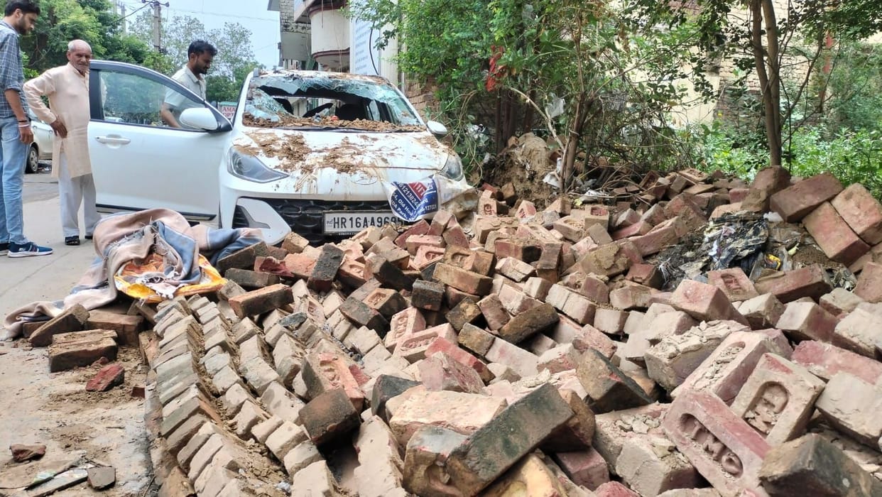 Car damaged and road blocked after wall collapses following rain.