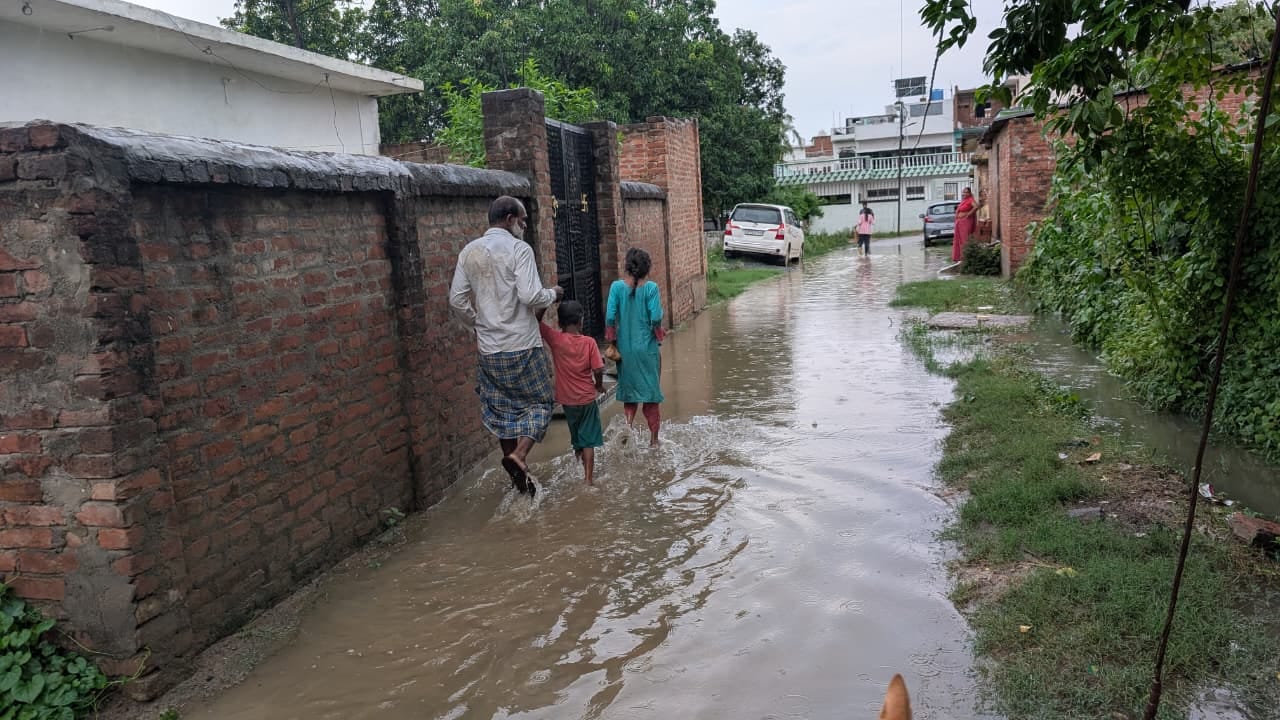 जलालपुर के जाफराबाद मोहल्ले में जलभराव के बीच से गुजरते लोग। संवाद