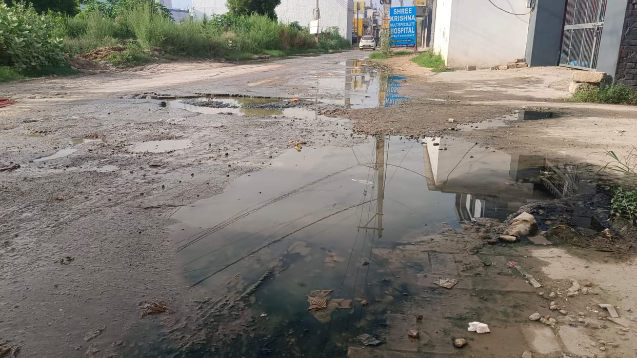 Contaminated water floods the road due to a clogged drain; commuters face inconvenience.