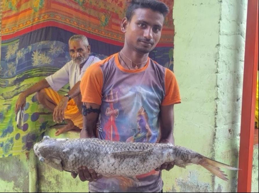 पंचप्रयाग तीर्थ में मरी मछली लेकर जाता युवक। संवाद