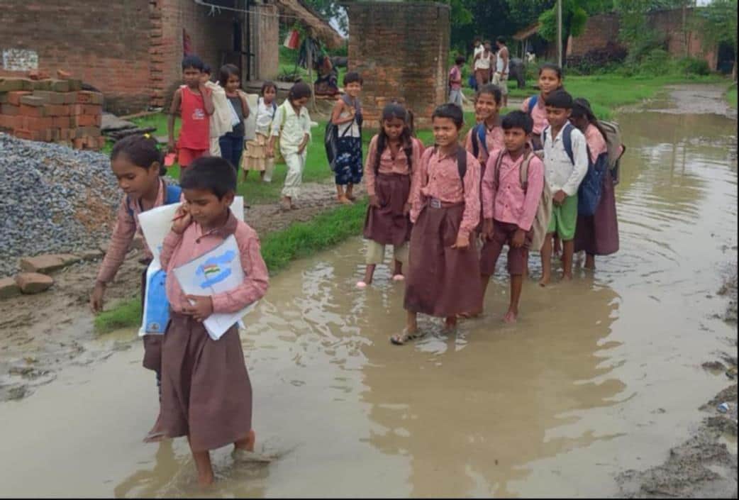 School children passing through a road that has turned into a pond