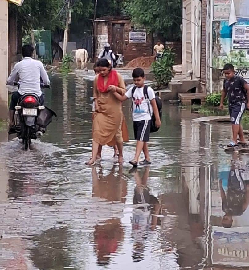 फोटो-1- शहर के मोहल्ला पीतांबर नगर में भरे पानी से बच्चे को लेकर निकलतीं महिला। संवाद
