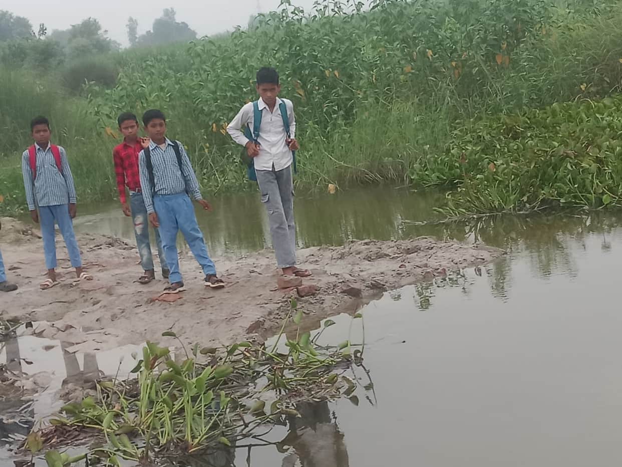 Students forced to wade through the filthy water of the Sivai drain due to the non-construction of a culvert.