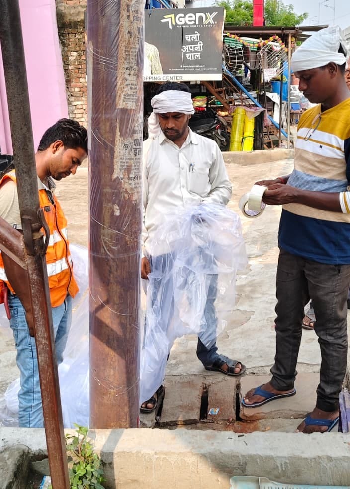महराजगंज में हाइवे के किनारे खंभे में प्लास्टिक लगाते निगम के कर्मचारी। संवाद