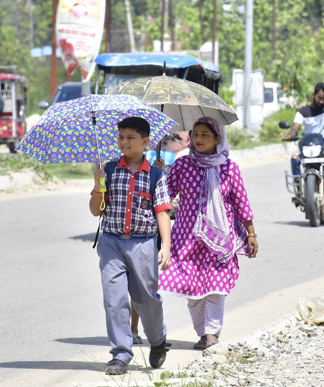 शहर के अशोक मार्ग पर स्कूल की छुट्टी होने के बाद बच्चों को छाते के सहारे घर ले जाती महिला।