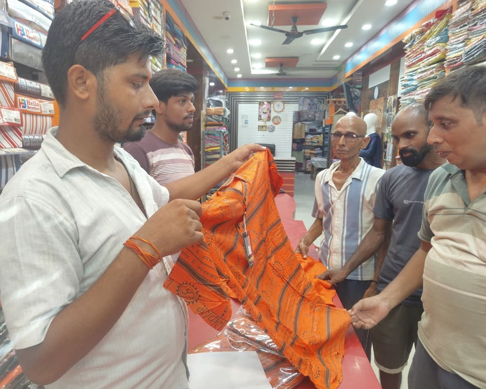  कांवड़ यात्रा के लिए कपड़े की दुकान पर भगवा टी-शर्ट पसंद करते लोग। संवाद