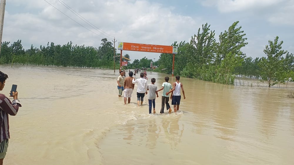 रहें हाथों में हाथ जलीलपुर क्षेत्र में सड़क पर बहते गंगा के पानी को पार करते युवक एक दूसरे का स
