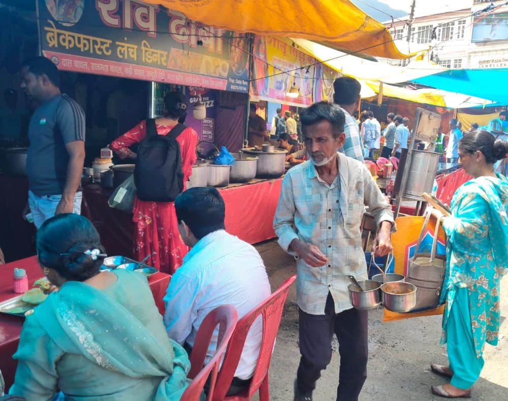 मिंजर मेले में दो नंबर चौगान में नंगे हाथों लोगों को खाना परोसता व्यक्ति । संवाद।