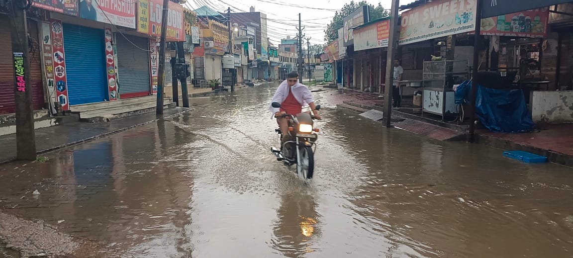 सिनेमा रोड पर जल भराव के बीच से गुजरा हुआ मोटरसाइकिल। संवाद