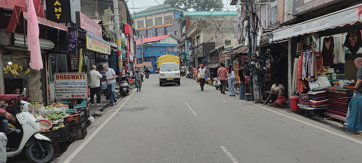 Shops extending up to the road and vehicles on the footpath.
