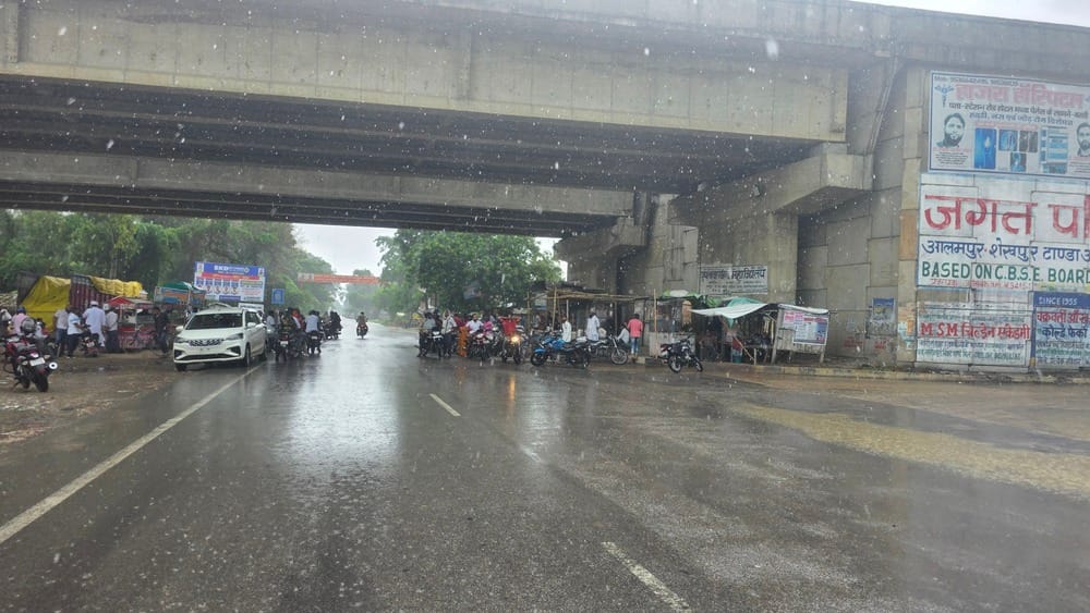 अकबरपुर टांडा मार्ग पर बृहस्पतिवार दोपहर बारिश के दौरान इनामीपुर फ्लाईओवर के नीचे इंतजार करते र