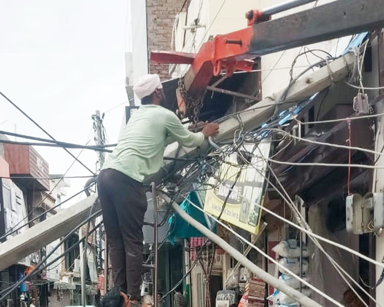 बिजली के गिरे पोल को ठीक करते कर्मचारी। संवाद
