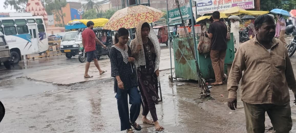 बारिश में जीटी रोड से छाता लगाकर गुजरती युवतियां। संवाद