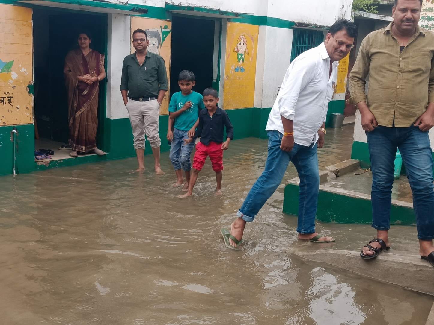 इलिया प्राथमिक विद्यालय में जलभराव से होकर गुजरते शिक्षक। स्रोत:-जागरूक पाठक
