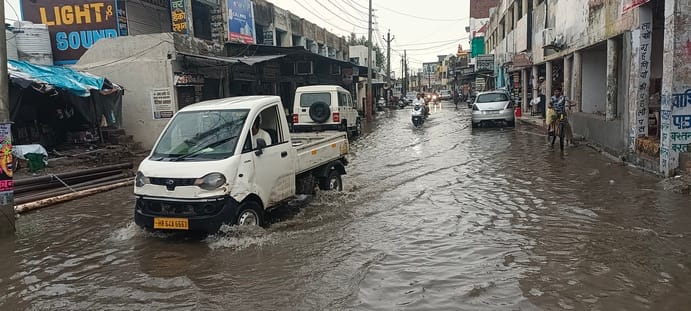 तेज बारिश के बाद चीका में सड़क पर जल भराव के बीच से गुजरते हुए वाहन। संवाद