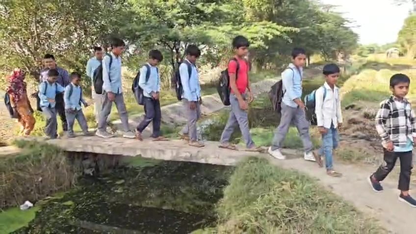 नाले पर बने बिजली के खंभे के पुल को पार कर स्कूल जाते बच्चे