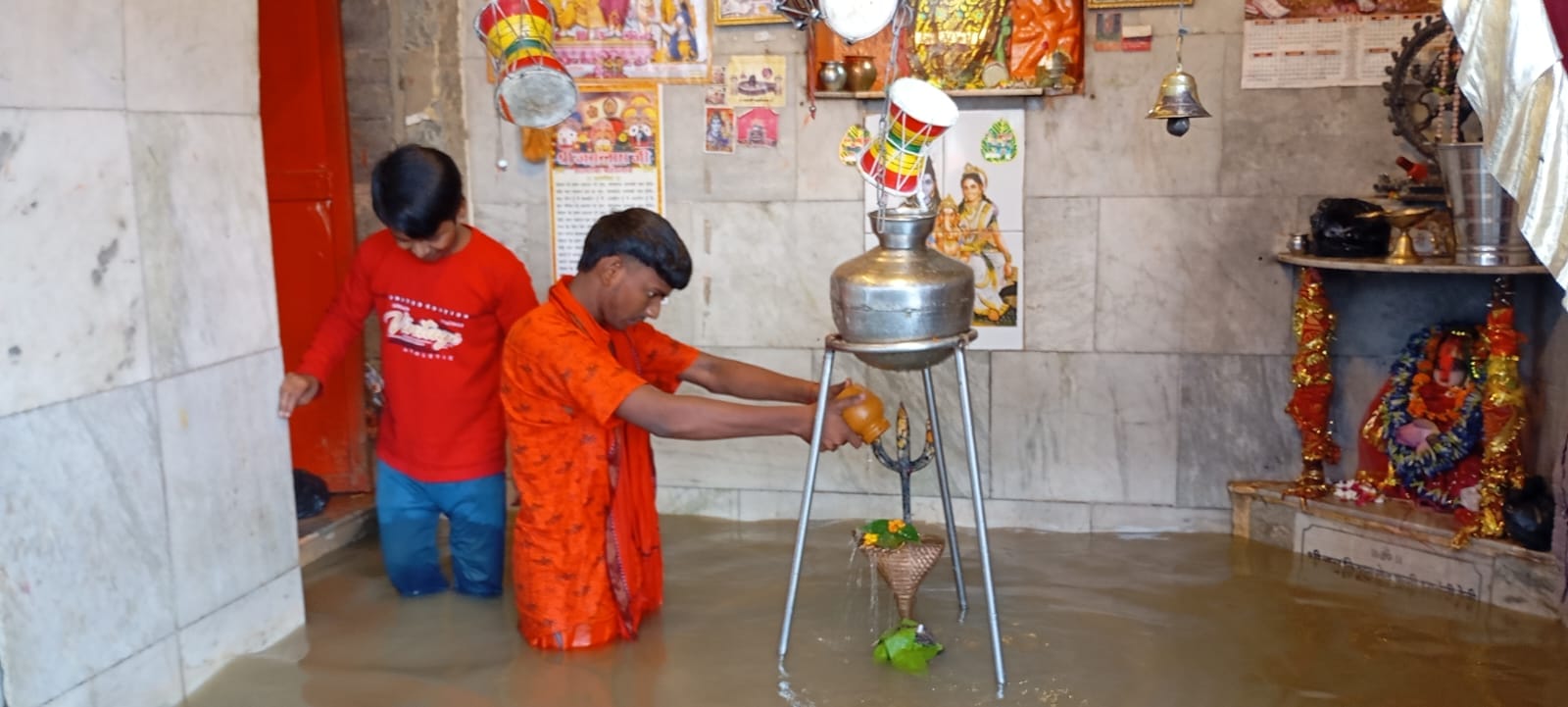 गोमती नदी के पानी से जलमग्न शिवलिंग पर जलाभिषेक करता शिवभक्त। संवाद