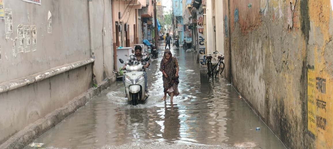 सोमवार को हुई बारिश के बाद मोहल्ला एमपी नगर में जलभराव के बीच निकलती महिला व स्कूटी सवार। संवाद