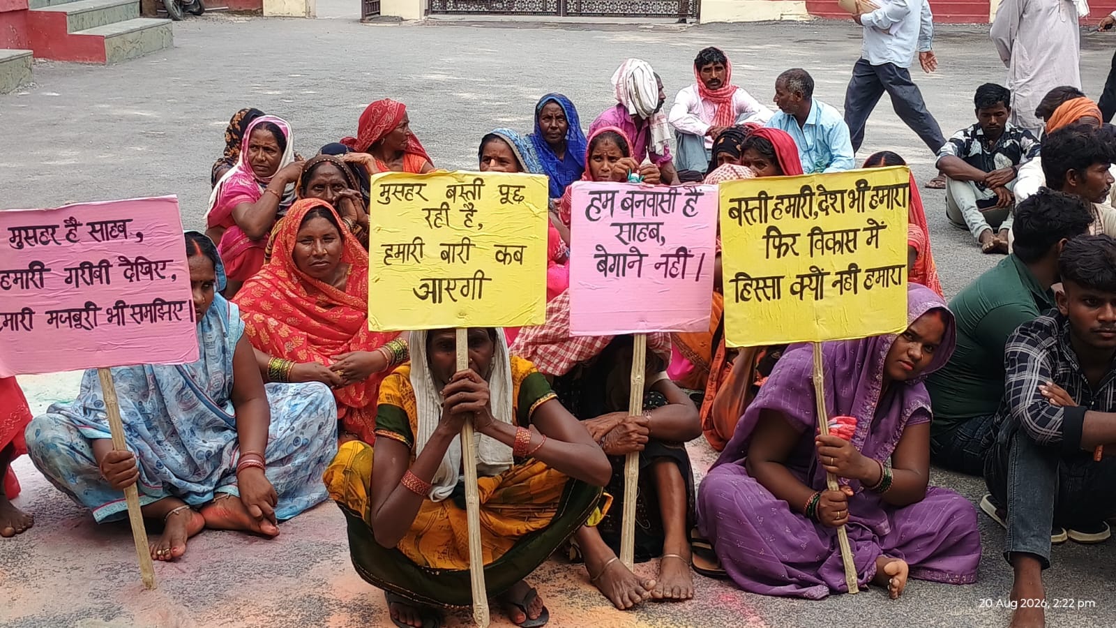 जिलाधिकारी कार्यालय परिसर में स्लोगन लिखी तख्ती के साथ बैठी रानीपुर के वनवासी बस्ती की महिलाएं।